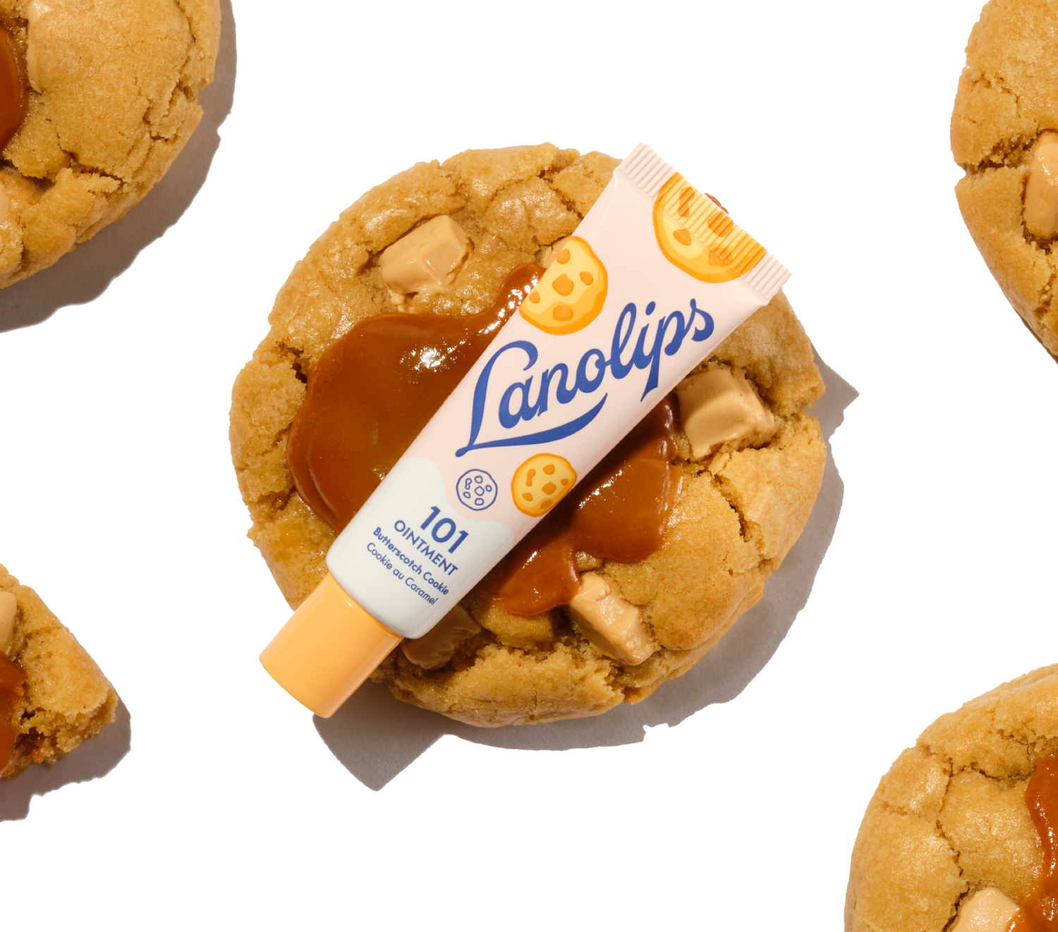 Lanolips 101 Multi-Balm Ointment in Butterscotch Cookie flavour. The 100% natural lanolin tube is layered over a thick, chewy biscuit topped with golden butterscotch and white chocolate chunks, part of the 101 Delicious collection.