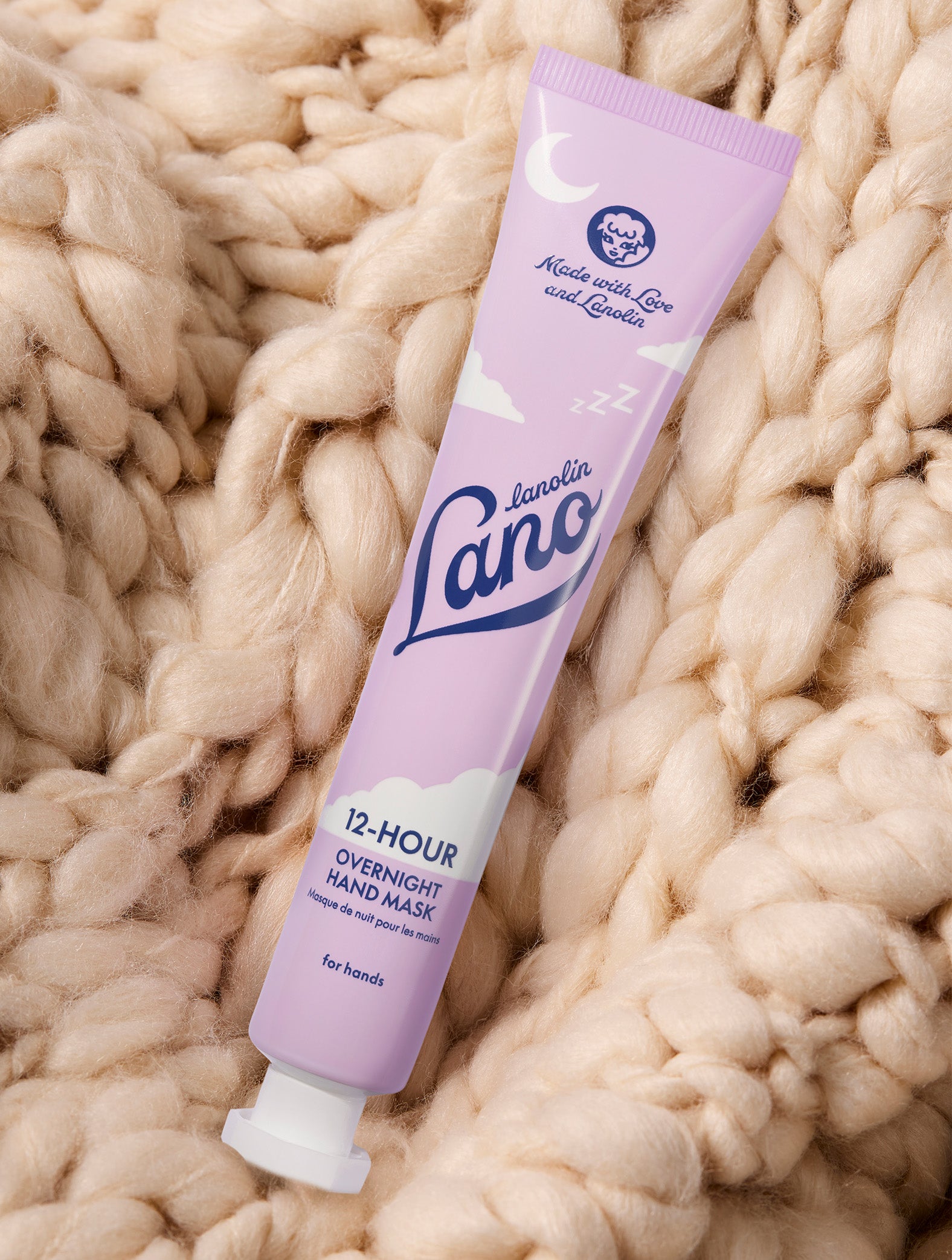 A tube of Lanolips 12 Hour Overnight Hand Mask placed on top of a wool blanket. Made with lanolin, ceramides, hyaluronic acid and vitamin-c to nourish your hands overnight. 