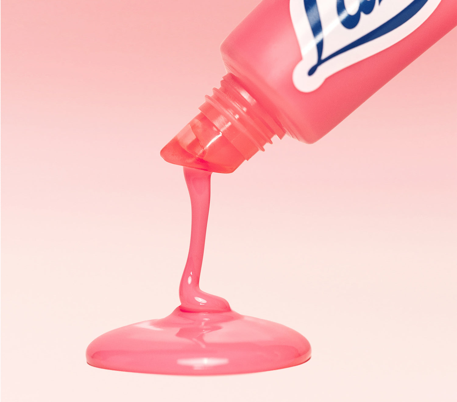 A close-up of Lanolips Milkshake Ceramide Balm in Strawberry Bubble, with a glossy pink balm being squeezed from the tube and pooling smoothly against a soft pink background.