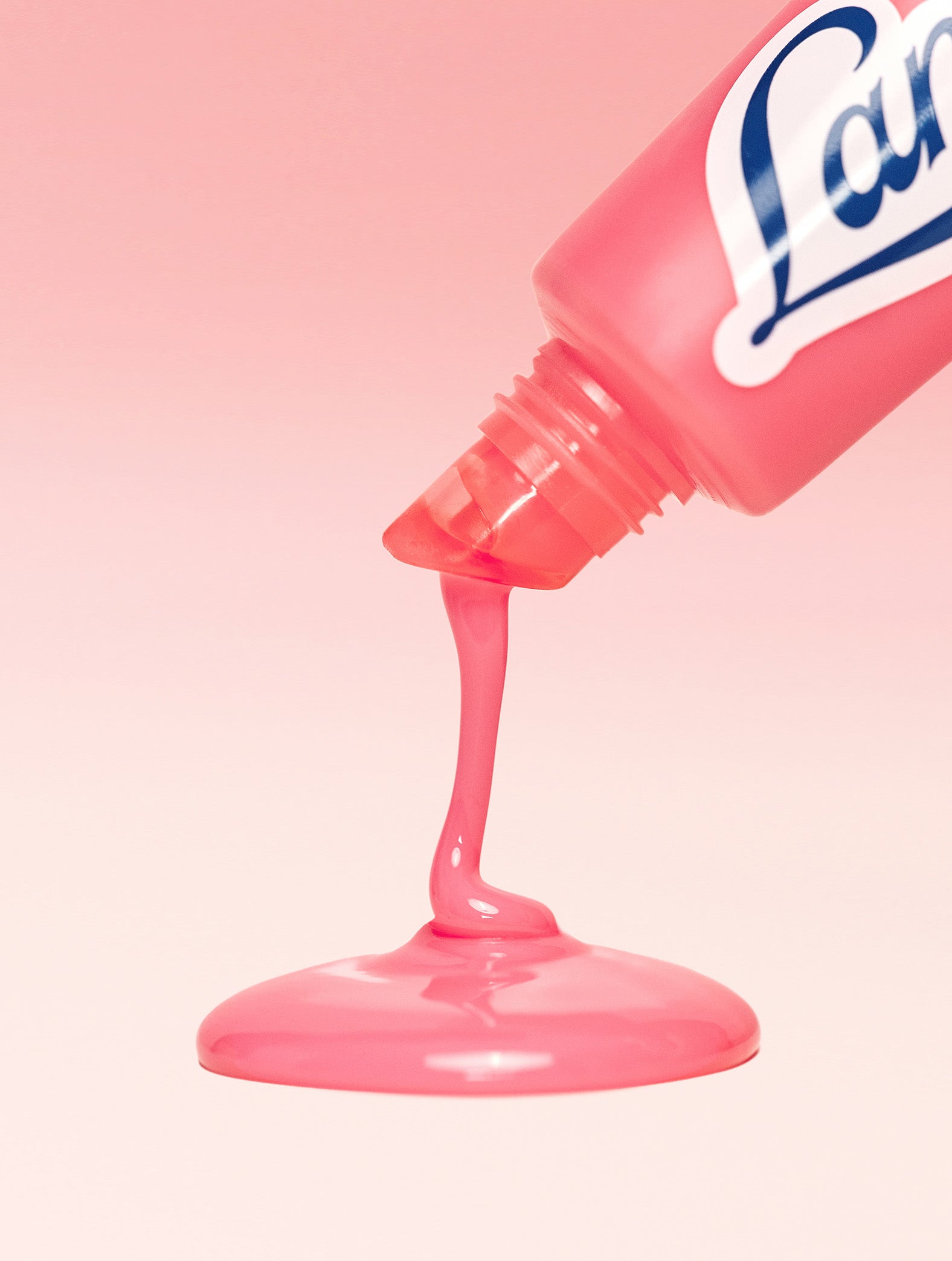 A close-up of Lanolips Milkshake Ceramide Balm in Strawberry Bubble, with a glossy pink balm being squeezed from the tube and pooling smoothly against a soft pink background.