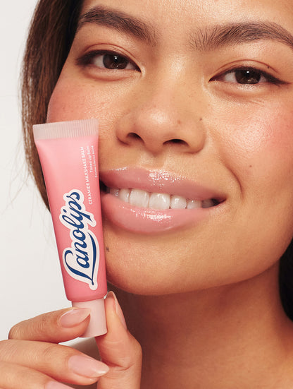 Model holding Lanolips Milkshake Ceramide Balm in Strawberry Bubble next to her face, showing glossy, hydrated lips with a soft strawberry pink finish.