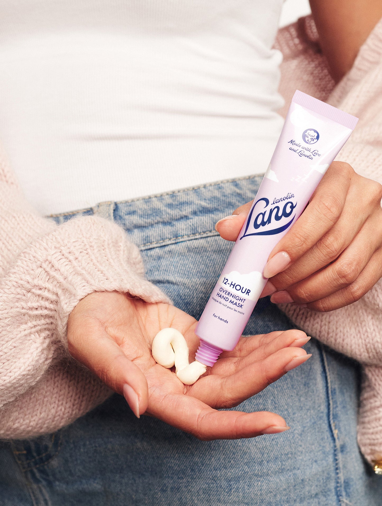 Close up shot of model squeezing a tube of Lanolips 12 Hour Overnight Hand Mask on their hand. In a thick and buttery formula combining hydrating lanolin and 
injected with mega actives including hyaluronic acid, ceramides and vitamin c,  it replenishes very dry skin while you sleep. 
