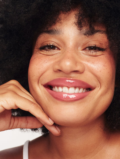 Close-up of smiling model with smooth, glossy lips wearing Lanolips Milkshake Ceramide Balm in Raspberry Crumble with a sheer raspberry tint